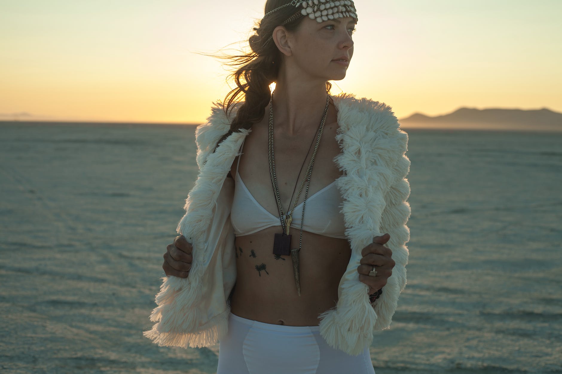 woman in white fur jacket and white skirt standing on beach during sunset